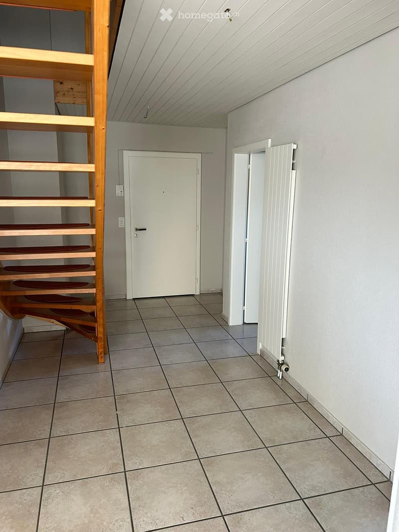Empty room with tiled floor, wooden shelving unit, white door, and radiator.