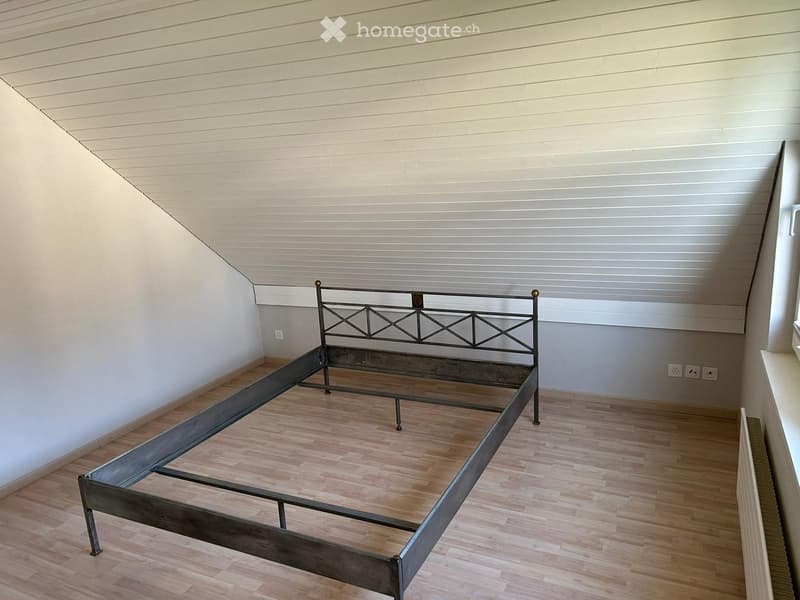 A room with wooden flooring and white walls, featuring a metal bed frame with a geometric headboard design.