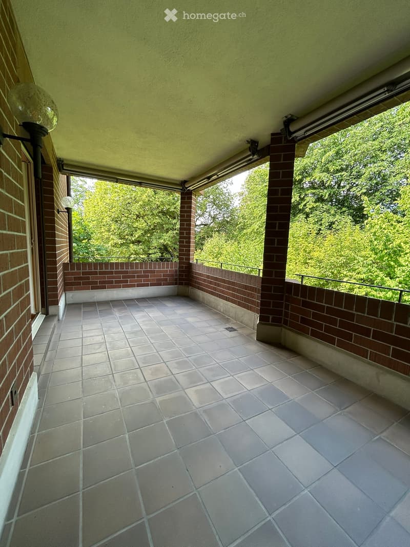 Balcony with tiled floor, brick walls, and metal railing, featuring a retractable awning and outdoor lighting.
