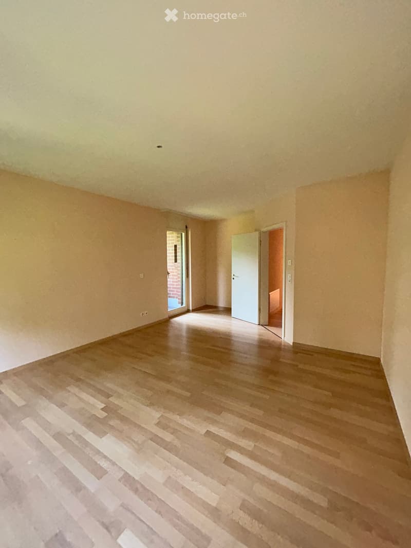 Empty room with light-colored walls and wooden flooring, featuring two open doors leading to adjacent spaces.