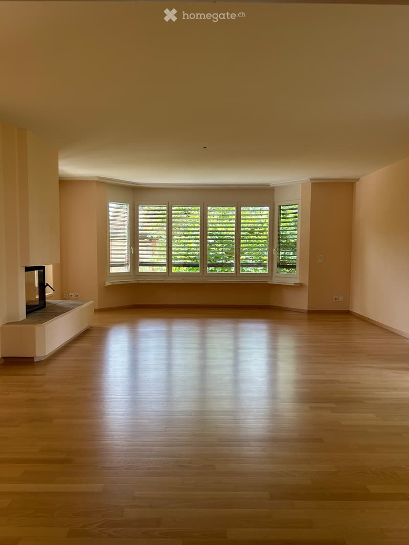 Empty room with wooden flooring, large windows with blinds, and a fireplace on the left side.