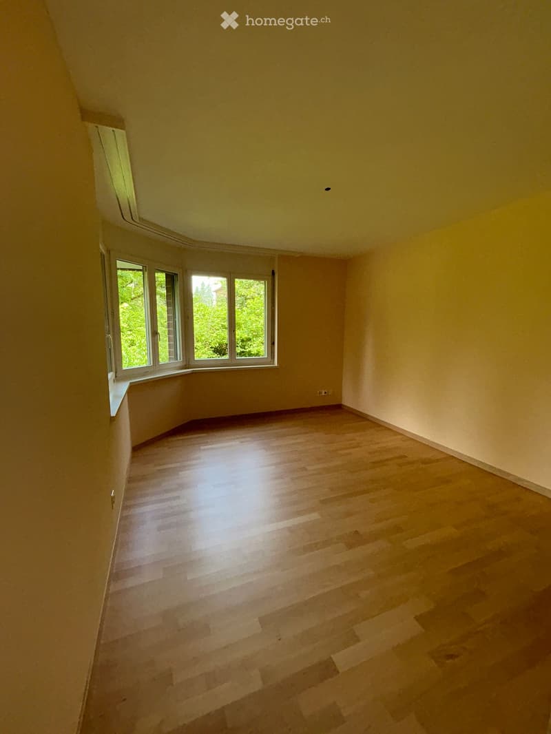 Empty room with wooden flooring and large windows letting in natural light. The walls are painted a light yellow color, and the ceiling is sloped, typical of an attic or loft space.