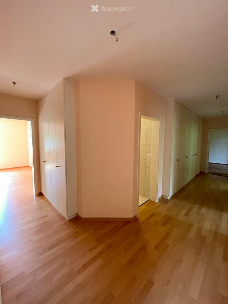 Empty hallway with wooden flooring, white walls, and several doors leading to other rooms.