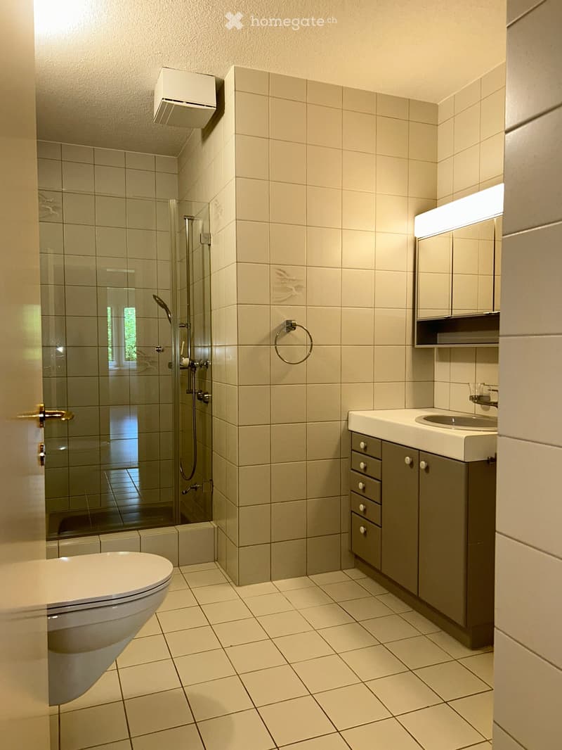 Modern bathroom with beige tiles, a toilet, a sink with a cabinet, a mirror, and a glass-enclosed shower area.