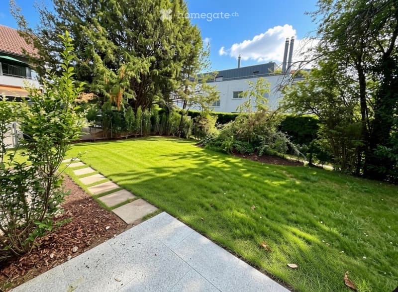 Well-maintained garden with a neatly trimmed lawn, stone pathway, and surrounding trees and shrubs.