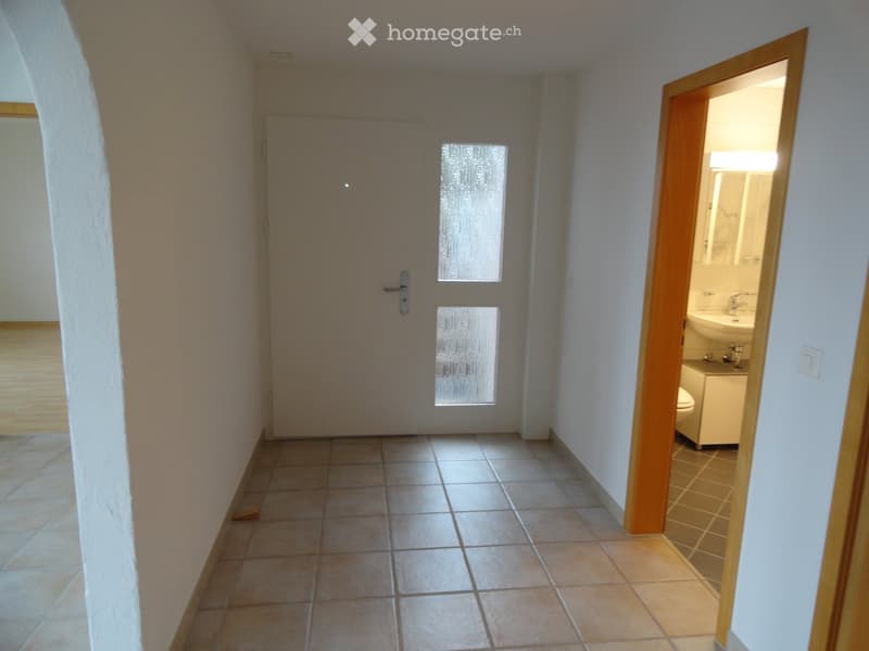 Empty hallway with tiled floor, white walls, and a partially open door leading to a small bathroom with a sink, toilet, and cabinet.