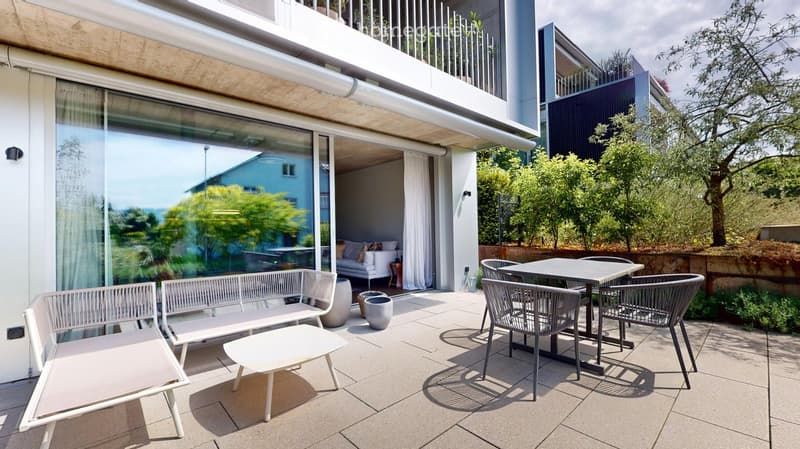 Modern outdoor terrace with a sofa, coffee table, dining table, chairs, and a bench, overlooking a green landscape.
