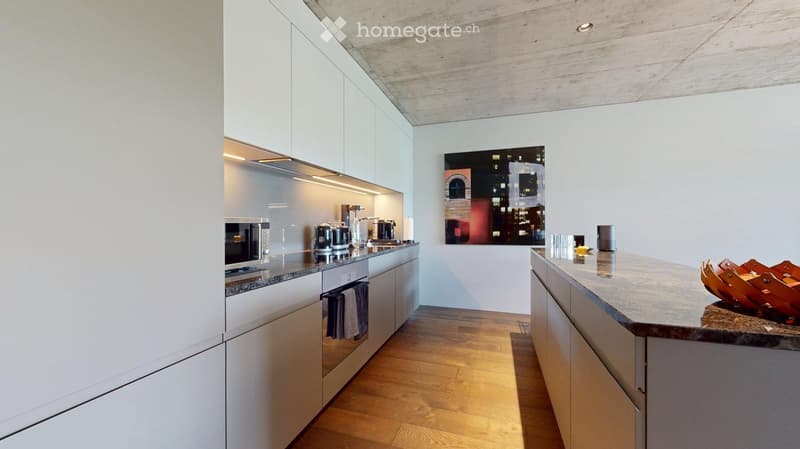 Modern kitchen with white cabinets, granite countertops, wooden flooring, and various appliances including a microwave, coffee maker, and oven. A cityscape painting adorns the wall.