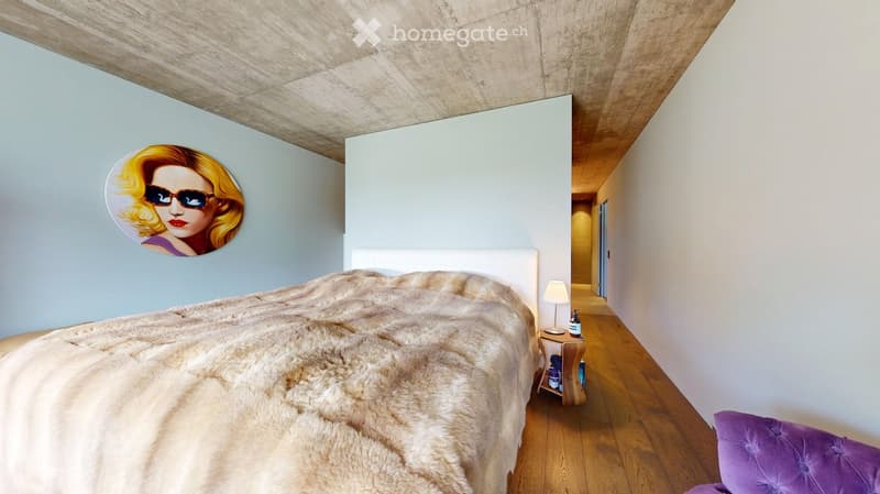 Modern bedroom with a large bed, fur throw, nightstand with lamp, and a decorative picture on the wall.