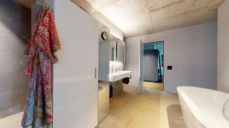 Modern bathroom with a freestanding bathtub, white sink, mirror, and cabinet. Light-colored tiles and wooden ceiling.