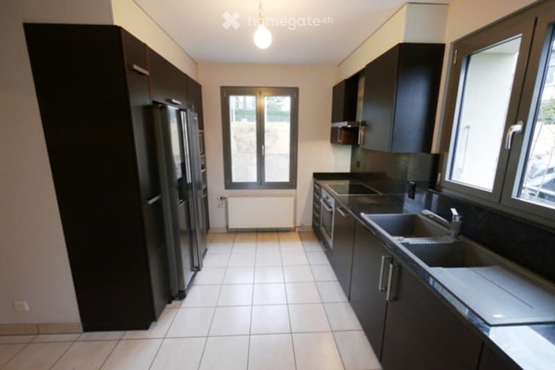 Modern kitchen with white tiled flooring, dark cabinets, stainless steel appliances, and large windows.