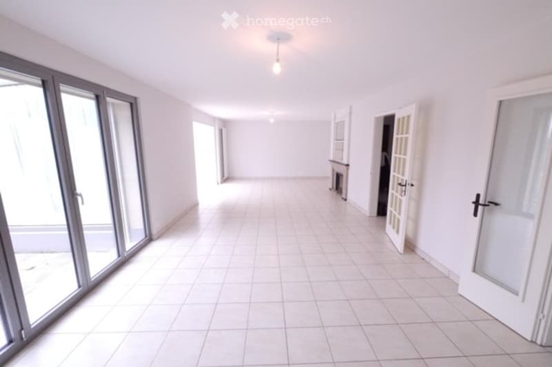 Empty hallway with tiled floor, white walls, large sliding glass doors, and several doorways leading to other rooms.