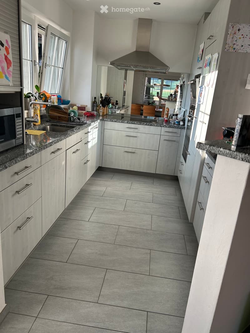Modern kitchen with white cabinets, granite countertops, and stainless steel appliances. Features a large island with a sink and microwave, and a range hood above the stove.