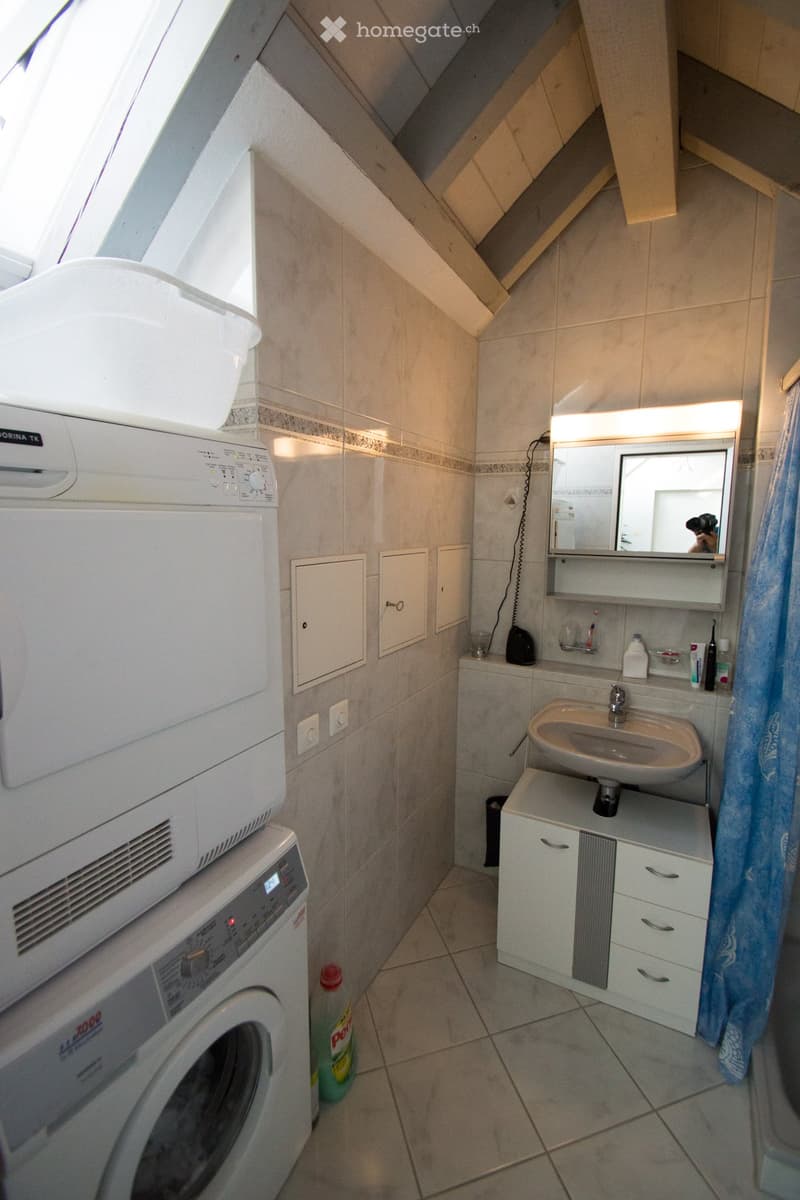 Bathroom with a sink, mirror, cabinet, washing machine, and a bottle on the floor.