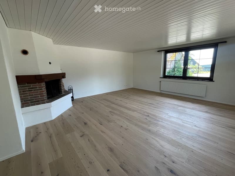 Empty room with wooden flooring, white walls, a fireplace, and a large window with blinds.