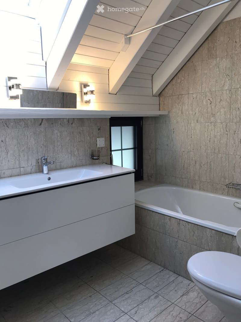 Modern bathroom with marble tiles, white sink, bathtub, toilet, and mirrored wall with built-in lighting.