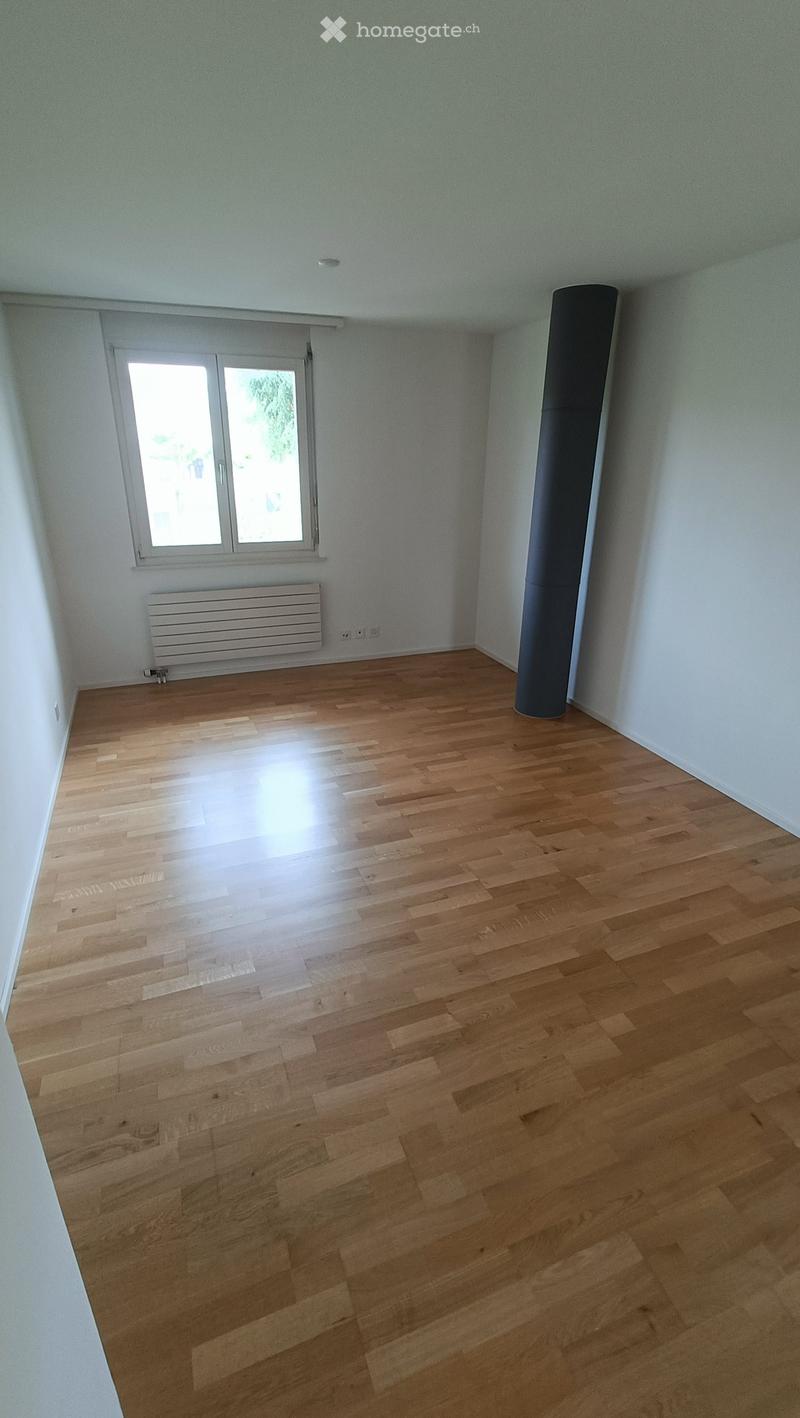Empty room with wooden flooring, white walls, a window with blinds, a radiator, and a black column.