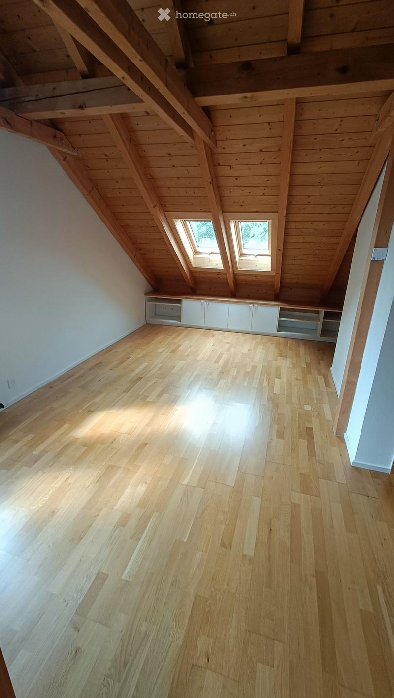 An empty attic space with wooden floors, exposed wooden beams, and skylights allowing natural light to enter.