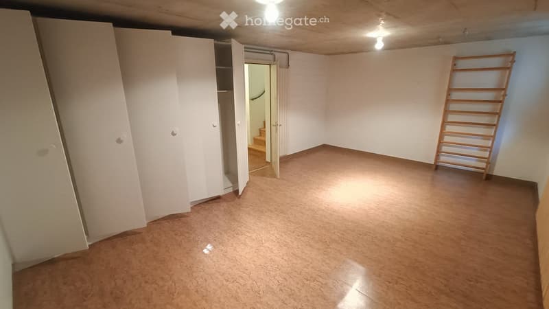 Empty room with wooden flooring, white walls, and a closet with open doors. A wooden ladder is leaning against the wall, and a doorway leads to another area.