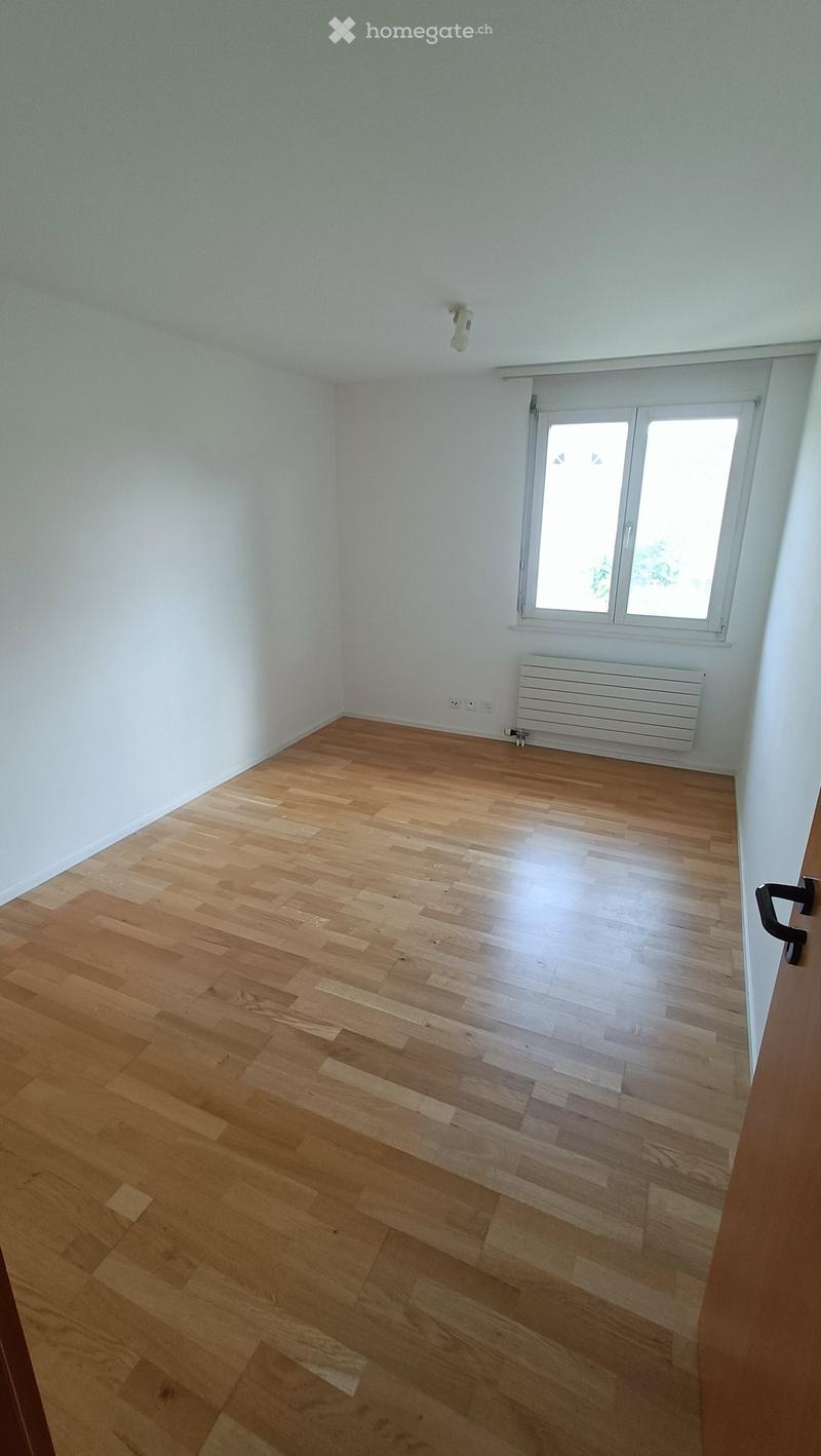 Empty room with light-colored wooden flooring, white walls, a window with white frame, and a white radiator below the window.