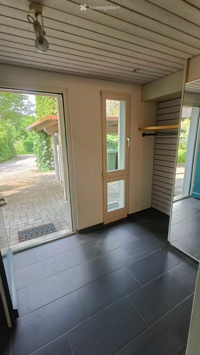 Empty room with dark tiled flooring, light-colored walls, and a large glass door leading to an outdoor area with greenery visible.