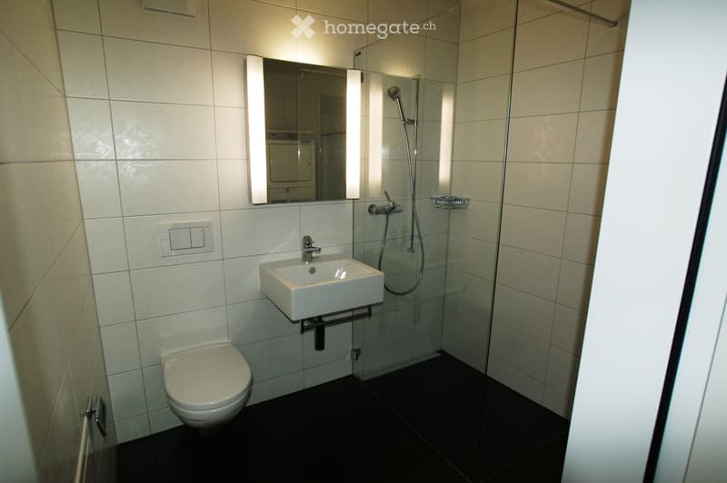 Modern bathroom with white tiles, a toilet, a sink with a mirror, and a glass-enclosed shower area.