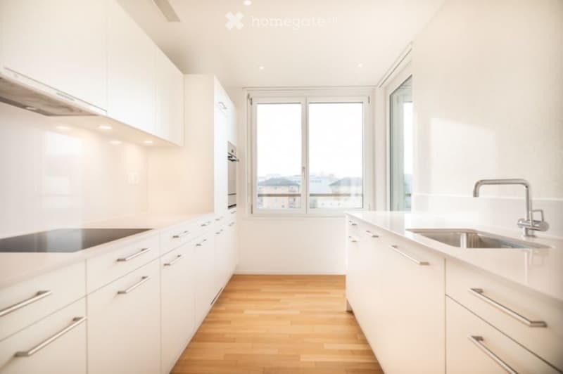 Modern, minimalist kitchen with white cabinets, stainless steel sink, and a large window offering a city view.
