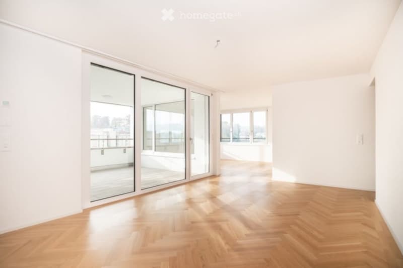 Empty room with wooden flooring, large glass sliding doors leading to a balcony, and a view of the city and sea.
