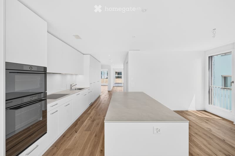 Modern kitchen with white cabinets, a central island, and a dark stainless steel oven. The space features wooden flooring and large windows allowing natural light to fill the room.