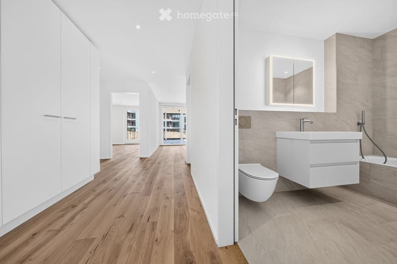 Modern hallway with light wooden flooring, white walls, built-in white cabinets, and a view into a contemporary bathroom featuring a floating sink, toilet, and mirror.