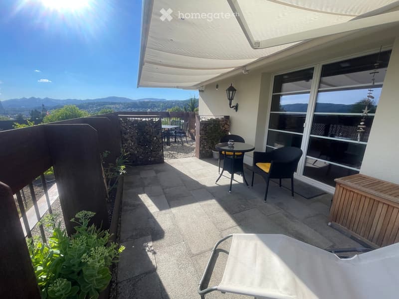 Balcony with a view, featuring a table, chairs, and a lounge chair, with a covered awning and a scenic mountain backdrop.