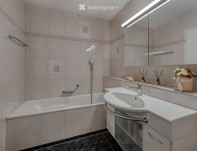 Modern bathroom with a bathtub, sink, large mirror, and decorative items on the counter.