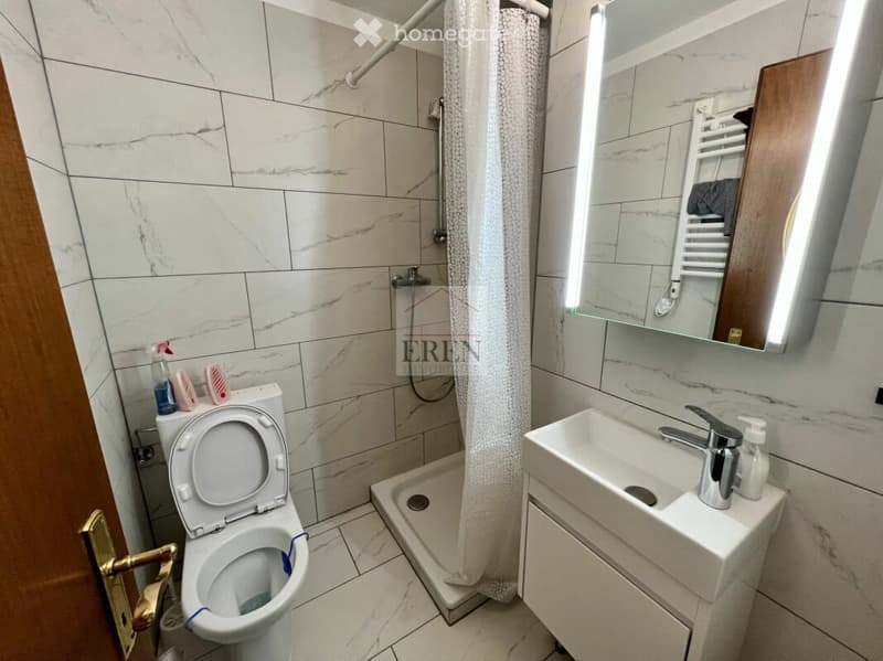 Modern bathroom with white marble tiles, a toilet, a sink with a mirror, and a shower with a curtain.