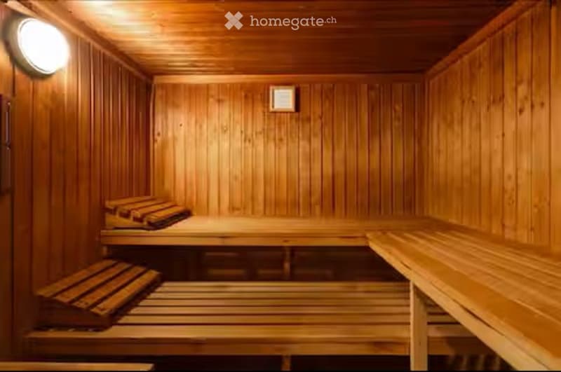 Wooden sauna with benches and stools, warm lighting, and a small framed picture on the wall.