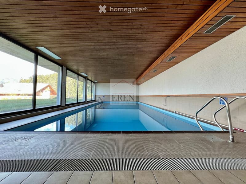 Indoor swimming pool area with large windows, wooden ceiling, and tiled floor.