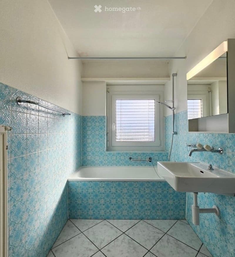 Bathroom with blue tiled walls and floor, bathtub, sink, mirror, and radiator.