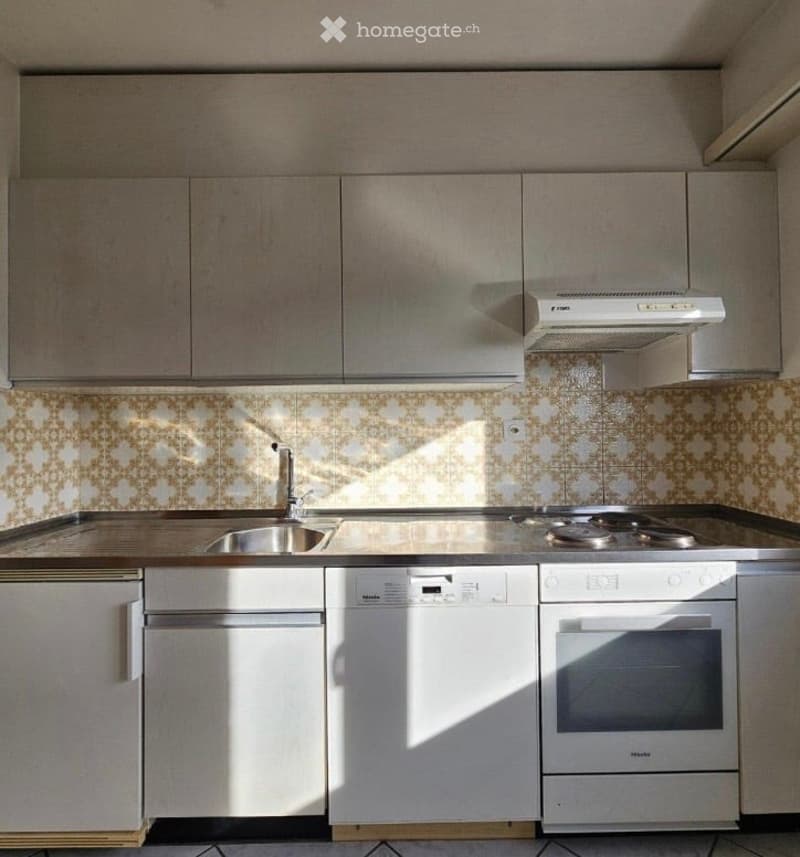 Modern kitchen with light grey cabinets, stainless steel appliances, and a patterned backsplash. Features a sink, stove, oven, and dishwasher.