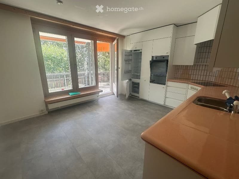 Modern kitchen with white cabinets, stainless steel appliances, and a large window opening to a balcony.