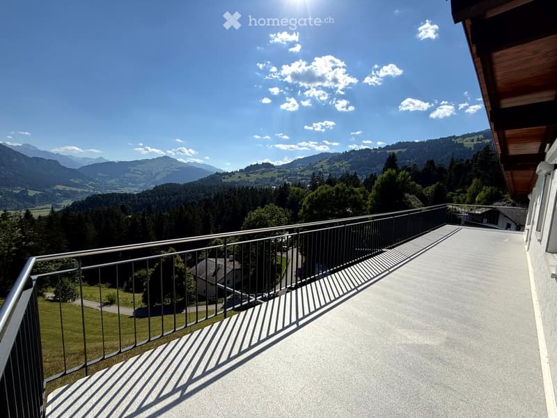 Balcony with metal railing, overlooking a scenic mountain landscape with trees and a house in the distance.