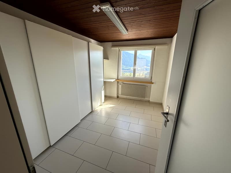 Empty room with tiled floor, white walls, wooden ceiling, and a window offering a mountain view.