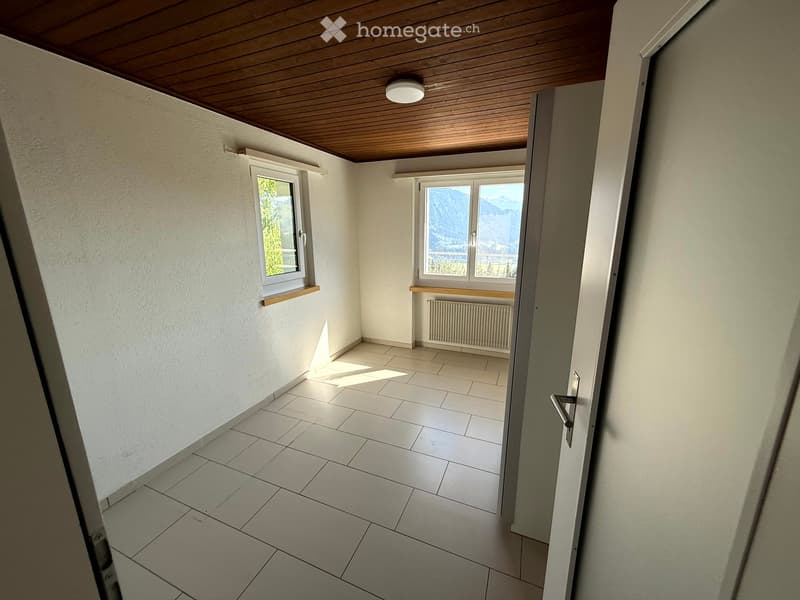 Empty hallway with tiled floor, white walls, wooden ceiling, and two windows offering a mountain view.