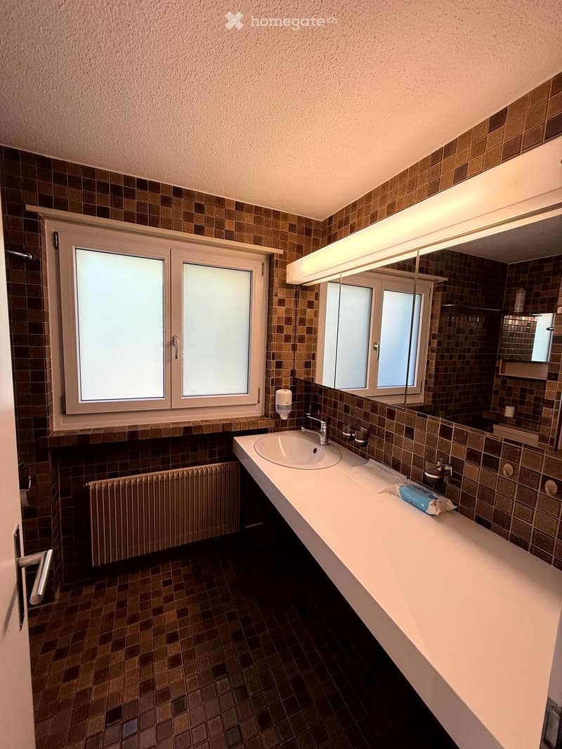 Bathroom with tiled walls and floor, a sink with a mirror above it, a radiator, and a window with frosted glass panes.
