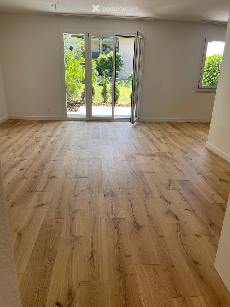 Empty room with light wooden flooring and large sliding glass doors leading to a garden area.