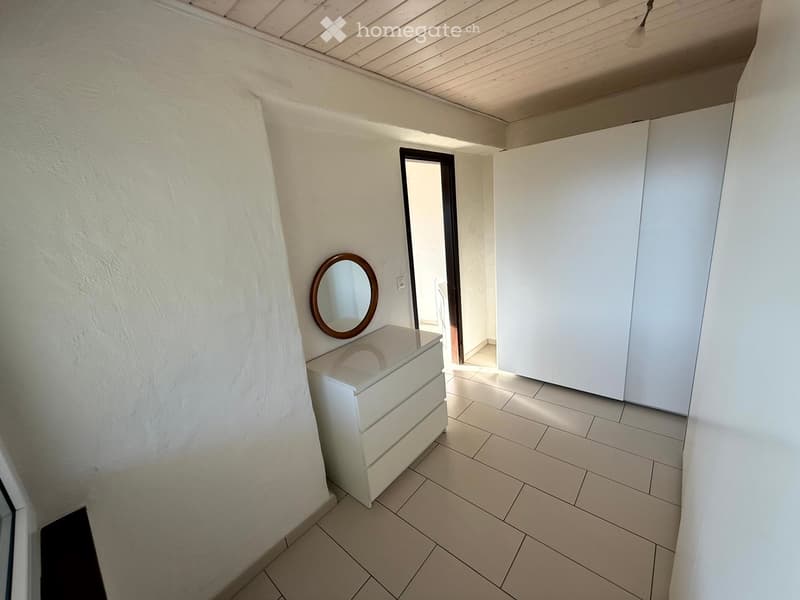 A small hallway with a white dresser, a round mirror, and a door leading to another room.