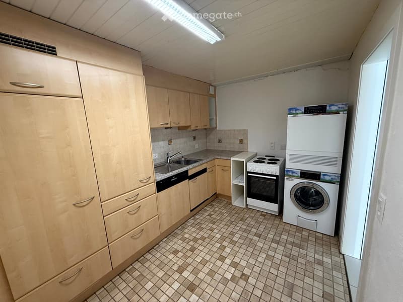 Compact kitchen with light wood cabinets, tiled floor, sink, oven, dishwasher, and washing machine.