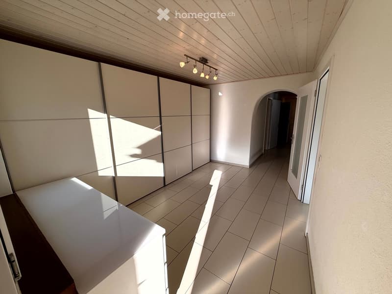 Bright, modern hallway with white tiled flooring, white walls, and built-in storage units. Features recessed lighting and an arched doorway leading to another room.