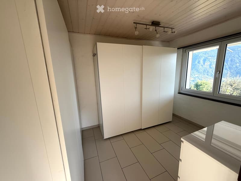 Empty room with white tiled floor, white built-in closet, large window with scenic mountain view, and recessed lighting fixture on the ceiling.