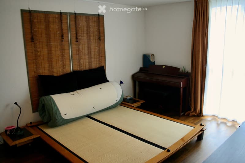 A cozy bedroom with tatami mats, a futon, a piano, and a small table with a lamp.