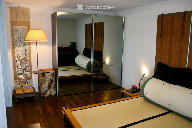 Modern bedroom with a tatami mat bed, large mirror, floor lamp, wicker basket, and decorative artwork on the wall.