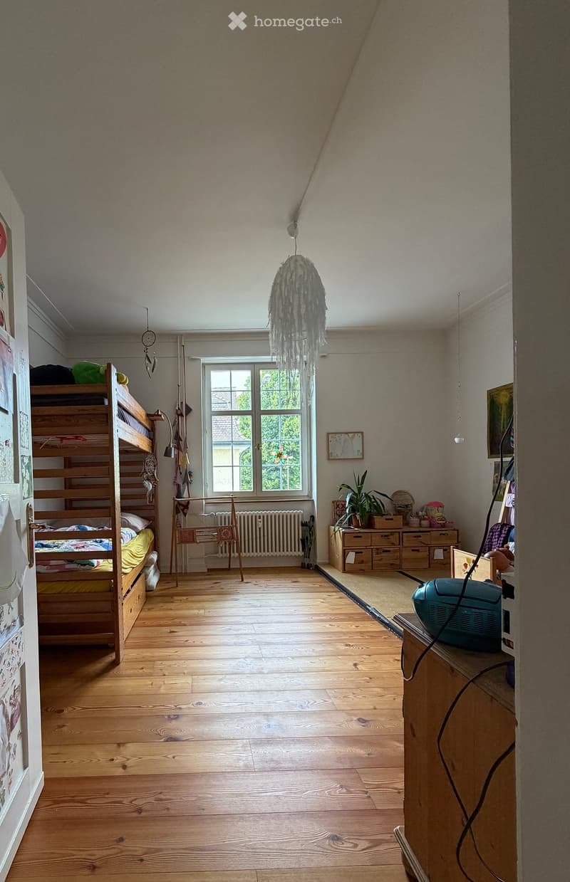 Cozy bedroom with wooden floors, bunk bed, storage unit, radiator, and a hanging lamp.